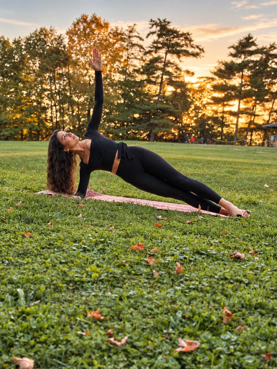 A side plank with one arm reaching upward during Pilates practice at sunset.